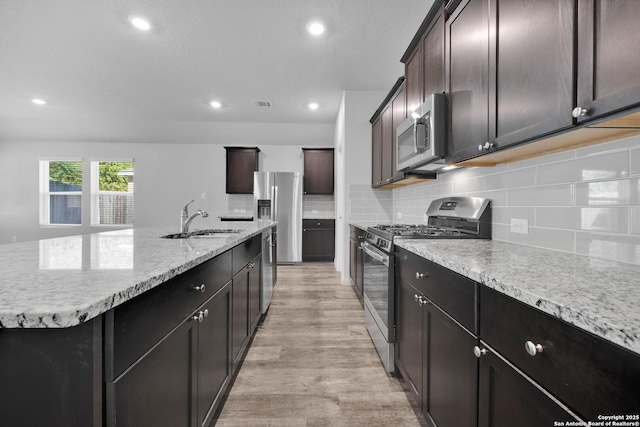 8559 Laxey Wheel, San Antonio, TX 78254 - kitchen with stainless steel appliances, a sink, a kitchen island with sink, light wood-style floors, and tasteful backsplash