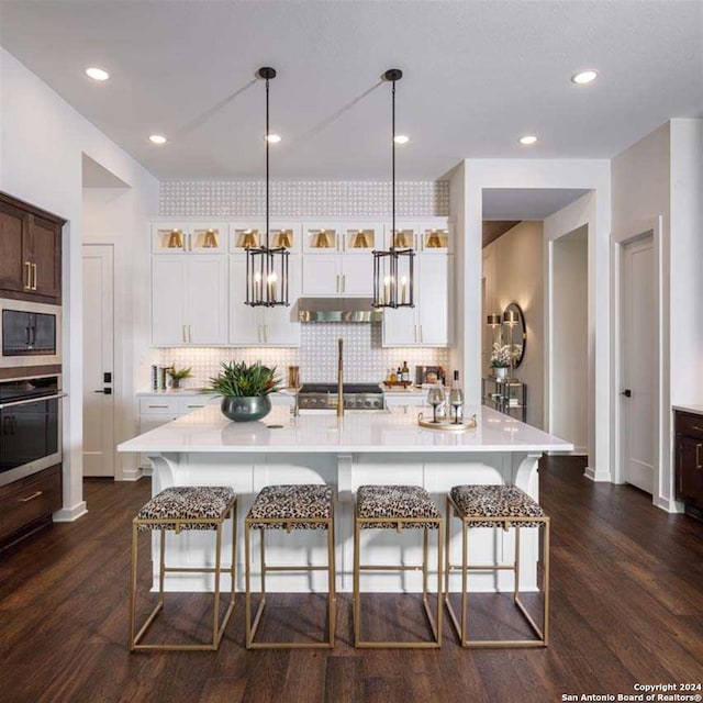 kitchen featuring oven, under cabinet range hood, decorative light fixtures, light countertops, and glass insert cabinets