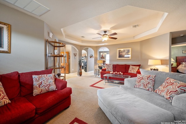 carpeted living room with ceiling fan and a raised ceiling