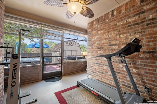 exercise area featuring ceiling fan and brick wall