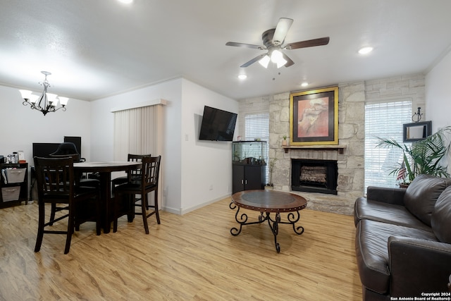 living room with ceiling fan with notable chandelier, a stone fireplace, ornamental molding, and light hardwood / wood-style flooring