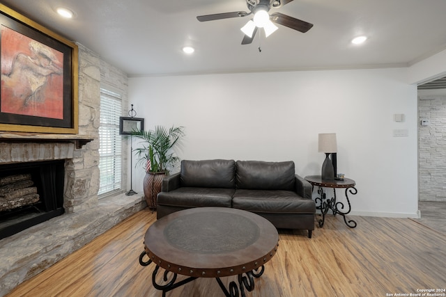 living room with ceiling fan, light hardwood / wood-style floors, a stone fireplace, and ornamental molding