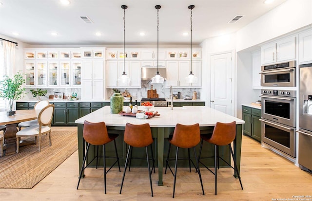 kitchen featuring an island with sink, a kitchen bar, glass insert cabinets, and light countertops