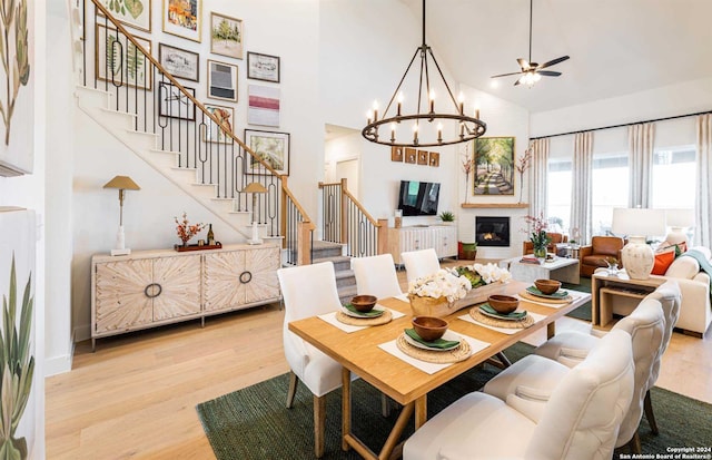 dining space featuring a glass covered fireplace, stairway, light wood-type flooring, high vaulted ceiling, and a notable chandelier