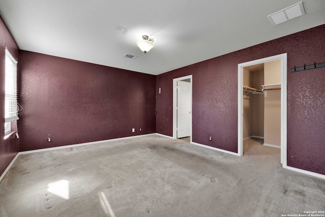 unfurnished bedroom featuring a walk in closet, light carpet, and a closet