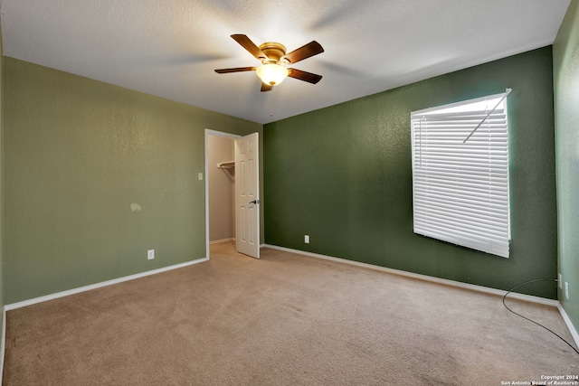 unfurnished bedroom with a textured ceiling, ceiling fan, a spacious closet, and light carpet