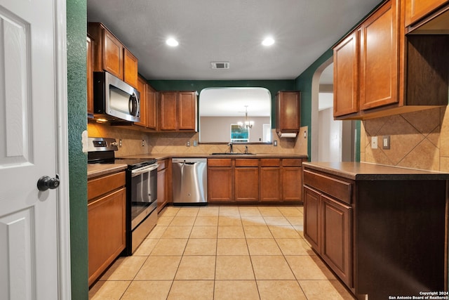 kitchen with backsplash, sink, light tile patterned floors, stainless steel appliances, and a chandelier