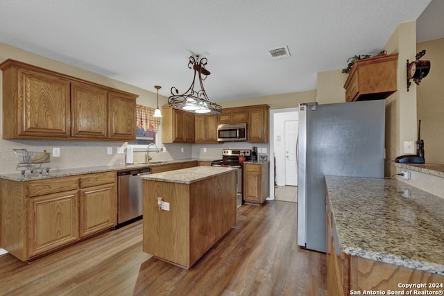 kitchen with sink, appliances with stainless steel finishes, decorative light fixtures, a kitchen island, and light wood-type flooring