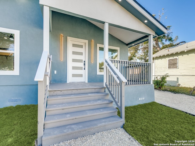 entrance to property featuring covered porch and a yard