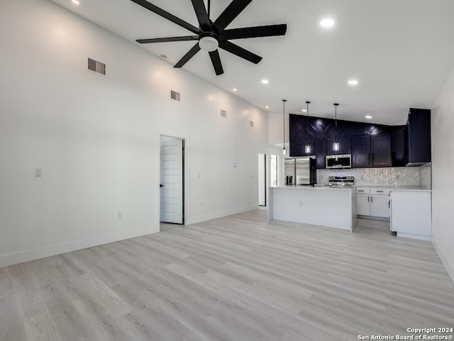 kitchen with ceiling fan, light hardwood / wood-style flooring, stainless steel appliances, and a high ceiling