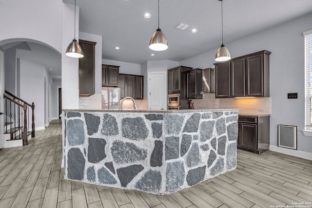 kitchen featuring dark brown cabinetry, wall chimney exhaust hood, light hardwood / wood-style floors, and decorative light fixtures