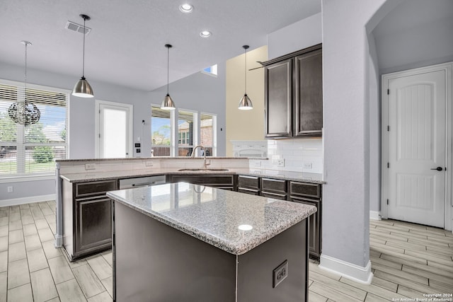 kitchen with light stone counters, dark brown cabinetry, sink, decorative light fixtures, and a center island