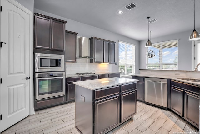 kitchen featuring sink, stainless steel appliances, wall chimney range hood, pendant lighting, and a kitchen island