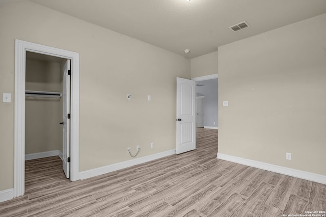 unfurnished bedroom with light hardwood / wood-style floors, a spacious closet, and a closet