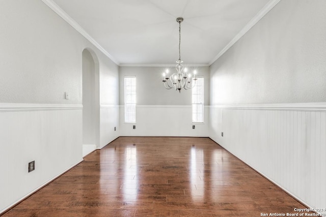 unfurnished dining area featuring wood-type flooring, crown molding, and an inviting chandelier