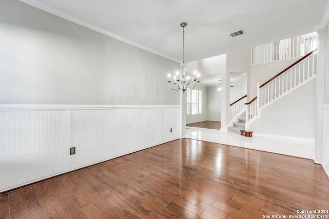 empty room featuring hardwood / wood-style floors, ornamental molding, and a chandelier