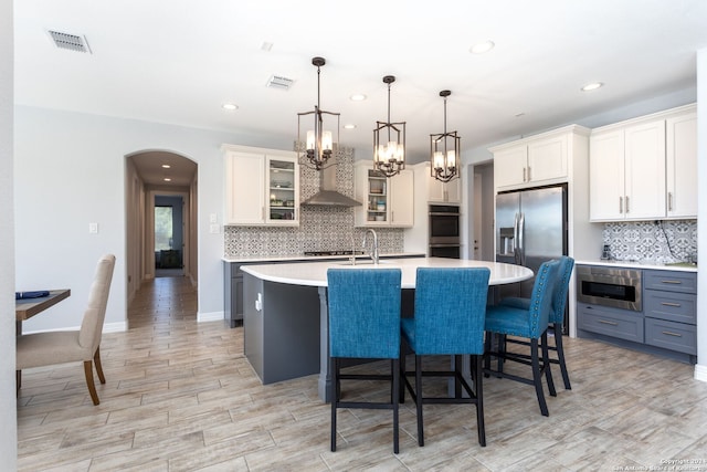 kitchen featuring a center island with sink, white cabinets, stainless steel appliances, and decorative light fixtures