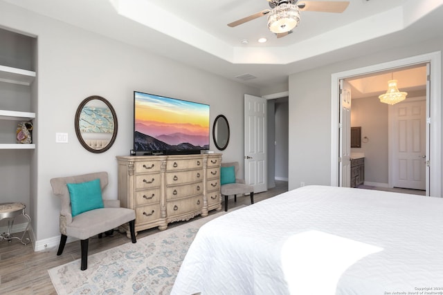 bedroom with a raised ceiling, ceiling fan, ensuite bathroom, and light hardwood / wood-style floors