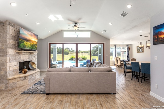 living room featuring ceiling fan, a stone fireplace, light wood-type flooring, and lofted ceiling