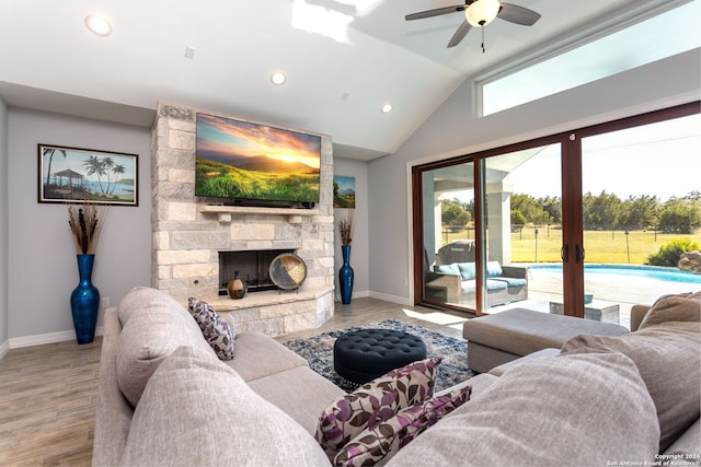 living room featuring lofted ceiling, ceiling fan, a stone fireplace, and light wood-type flooring