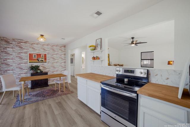 kitchen featuring ceiling fan, light hardwood / wood-style flooring, brick wall, stainless steel electric stove, and white cabinets