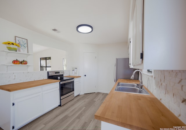 kitchen with appliances with stainless steel finishes, light wood-type flooring, sink, white cabinets, and butcher block counters