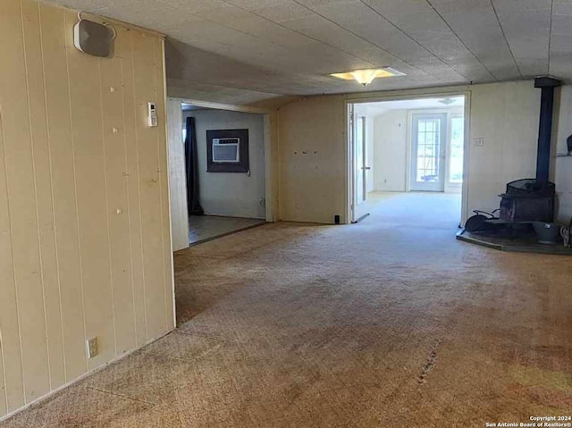 spare room featuring light colored carpet, a wood stove, an AC wall unit, and wood walls