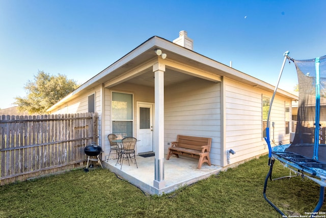 rear view of property with a patio, a trampoline, and a lawn