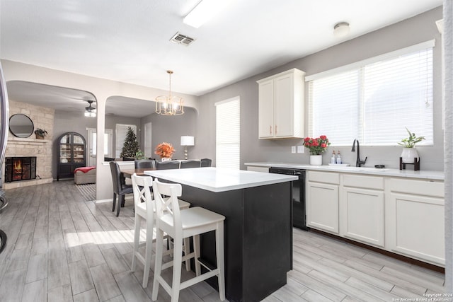 kitchen featuring dishwasher, white cabinets, a stone fireplace, light hardwood / wood-style flooring, and decorative light fixtures