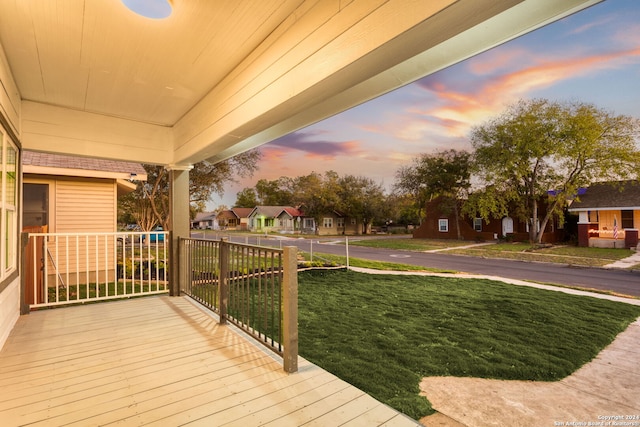 deck at dusk with a lawn and covered porch