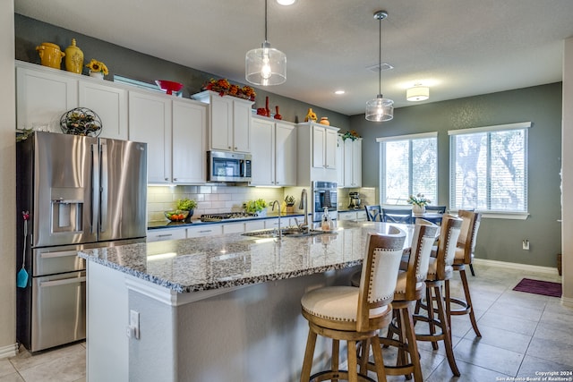 kitchen with pendant lighting, white cabinetry, stainless steel appliances, and an island with sink