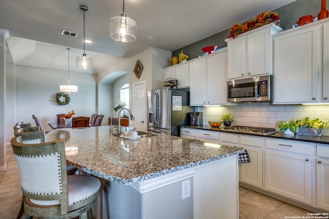 kitchen with sink, an island with sink, stainless steel appliances, and decorative light fixtures