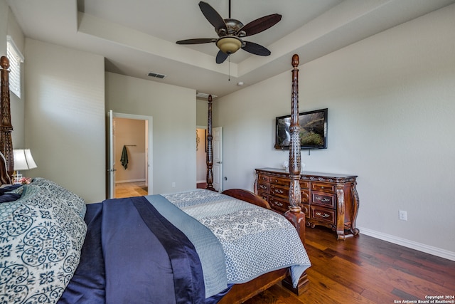 bedroom with ensuite bathroom, a raised ceiling, dark hardwood / wood-style floors, and ceiling fan