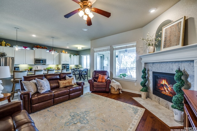 living room with ceiling fan, a fireplace, wood-type flooring, and a textured ceiling