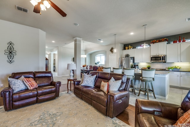 living room with ceiling fan, a textured ceiling, and light hardwood / wood-style flooring