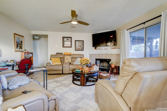 living room with light carpet, a textured ceiling, ceiling fan, and a tiled fireplace