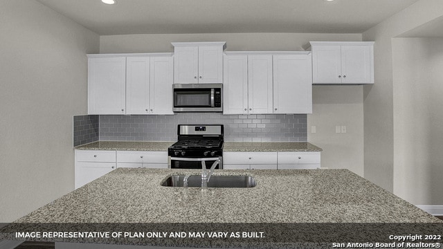 kitchen with appliances with stainless steel finishes, backsplash, light stone counters, sink, and white cabinets