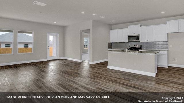 kitchen with appliances with stainless steel finishes, dark hardwood / wood-style flooring, a center island with sink, and white cabinetry