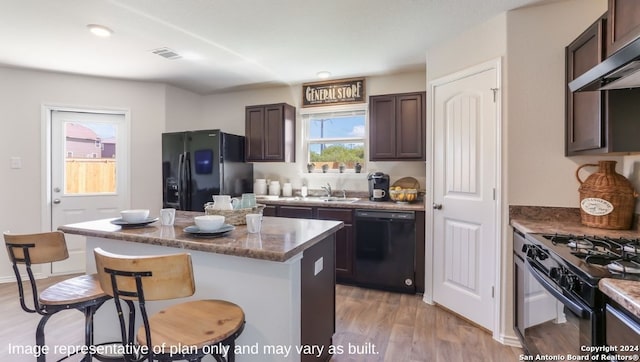 kitchen featuring ventilation hood, black appliances, light hardwood / wood-style flooring, a center island, and a breakfast bar area