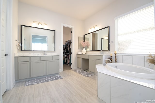 bathroom with tiled bath, a wealth of natural light, and vanity