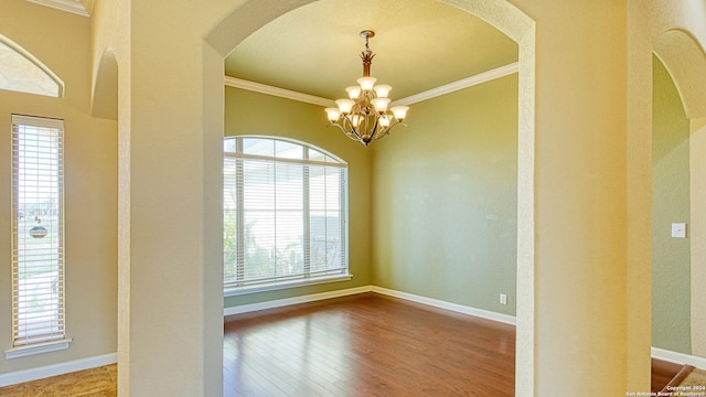 spare room with hardwood / wood-style flooring, a healthy amount of sunlight, ornamental molding, and a chandelier