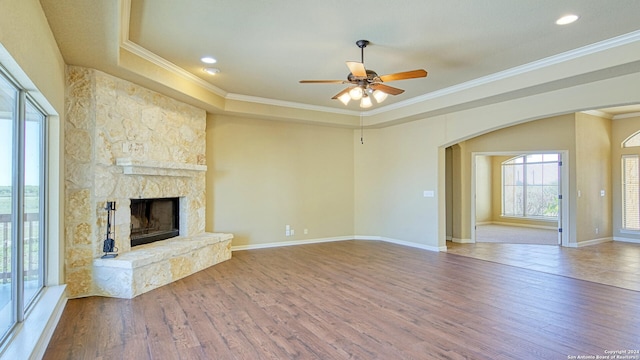 unfurnished living room featuring ornamental molding, a tray ceiling, ceiling fan, a fireplace, and hardwood / wood-style floors