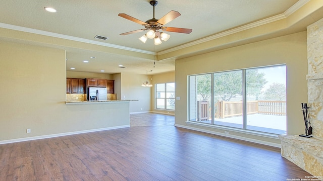 unfurnished living room featuring dark hardwood / wood-style flooring, ceiling fan with notable chandelier, a textured ceiling, a raised ceiling, and crown molding