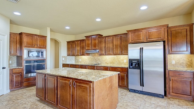 kitchen featuring light stone countertops, decorative backsplash, stainless steel appliances, and a kitchen island