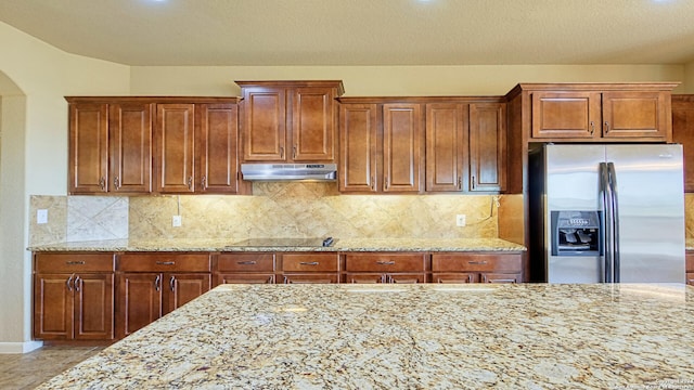 kitchen with light stone counters, stainless steel refrigerator with ice dispenser, a textured ceiling, black electric cooktop, and decorative backsplash