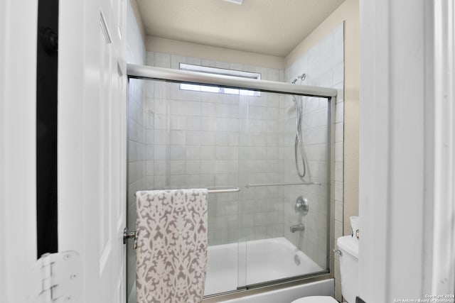 bathroom featuring combined bath / shower with glass door, a textured ceiling, and toilet