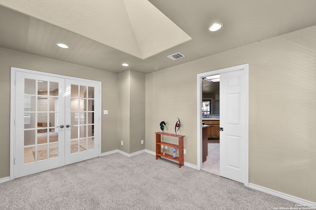 spare room with french doors, a textured ceiling, and light colored carpet