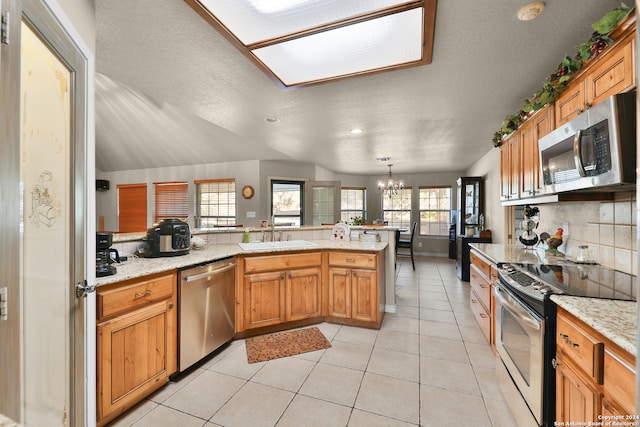 kitchen with a notable chandelier, kitchen peninsula, stainless steel appliances, and a wealth of natural light