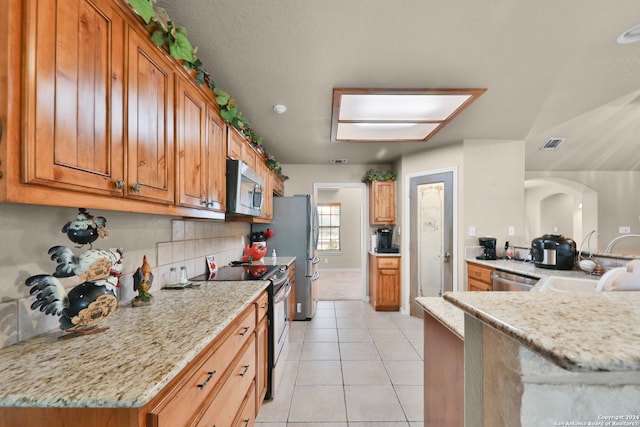 kitchen with sink, tasteful backsplash, light stone counters, light tile patterned floors, and appliances with stainless steel finishes