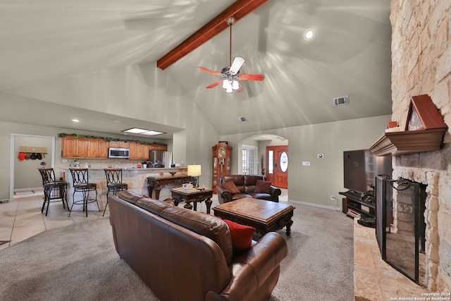 living room featuring light colored carpet, ceiling fan, beam ceiling, high vaulted ceiling, and a stone fireplace